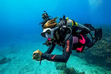a female diver swims past the camera underwater. he tank shows the green and yellow nitrox sticker