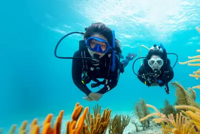 two female scuba divers swim over a soft coral reef in clear water