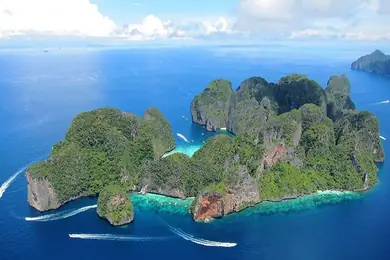an aerial view of a tropical island covered with vegetation and surrounded by blue water. Many small boats explore many bays and beaches