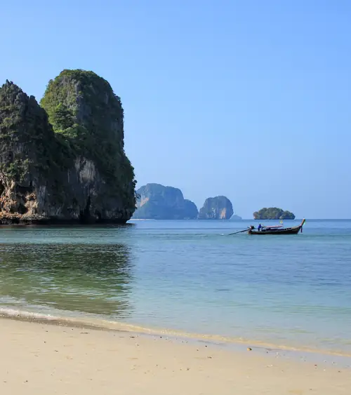 a sandy beach with blue sea and sky limestone cliffs and traditional wooden fishing boat