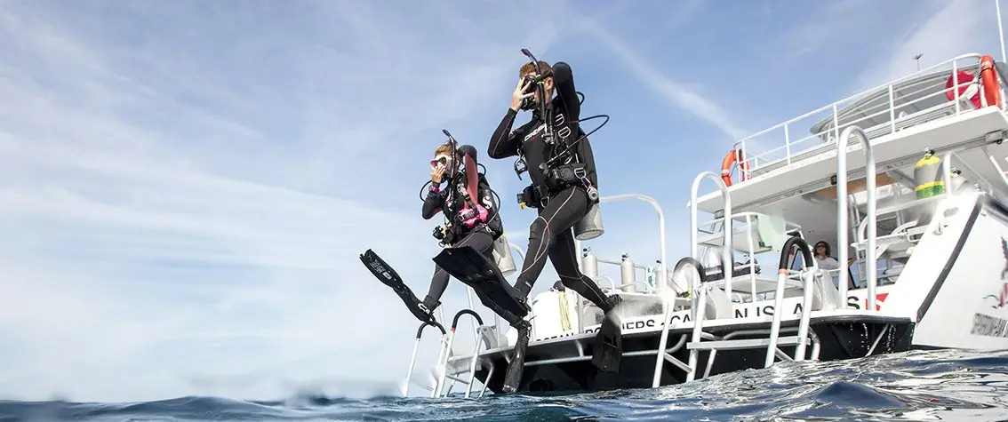 two scuba divers giant stride step off the back of diving boat deck 