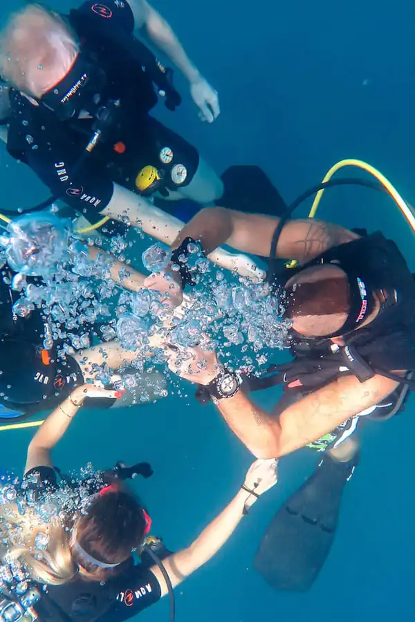 a group of four scuba divers preparing and signaling to ascend to the water surface