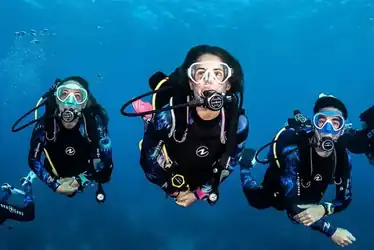 three scuba divers in a group swim gracefully towards the camera