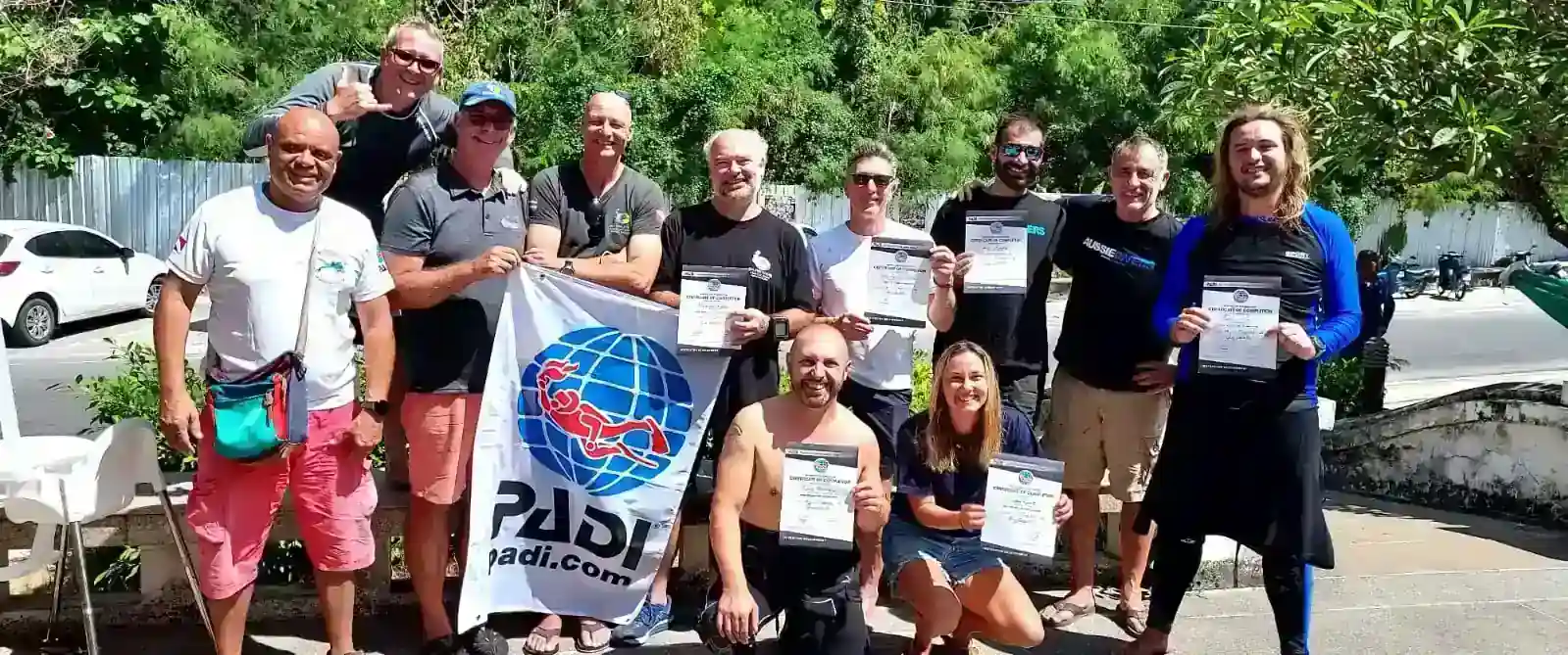 A group of people pose for a group photo with their now PADI Instructor Certificates.